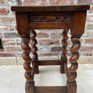 May include: A small, antique wooden side table with a rectangular top and intricately carved, spiral-turned legs. The table is made of dark-stained wood, showcasing the natural grain. The design includes a decorative panel below the tabletop, adding to its vintage charm.