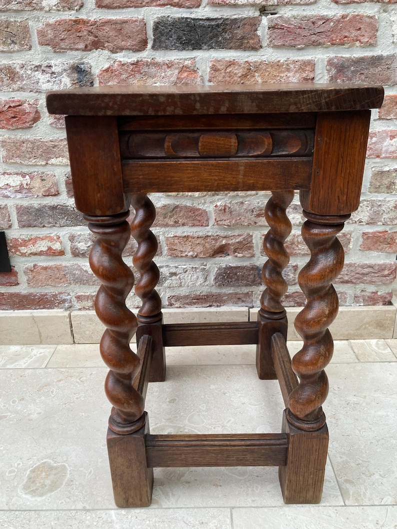 May include: A small, antique wooden side table with a rectangular top and intricately carved, spiral-turned legs. The table is made of dark-stained wood, showcasing the natural grain. The design includes a decorative panel below the tabletop, adding to its vintage charm.