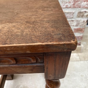 May include: A close-up of a wooden side table with a rectangular top and a carved apron. The table has a turned leg with a spiral design. The wood has a warm, brown tone and visible grain.