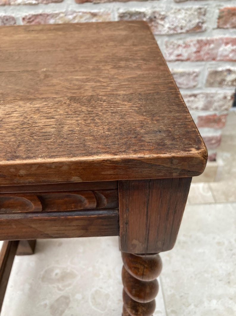 May include: A close-up of a wooden side table with a rectangular top and a carved apron. The table has a turned leg with a spiral design. The wood has a warm, brown tone and visible grain.