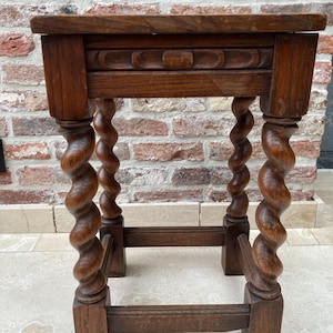 May include: A small, antique wooden side table with a dark brown finish. The table features a rectangular top, a carved apron, and four intricately carved, spiral-turned legs. The legs are connected by a lower stretcher for added stability.