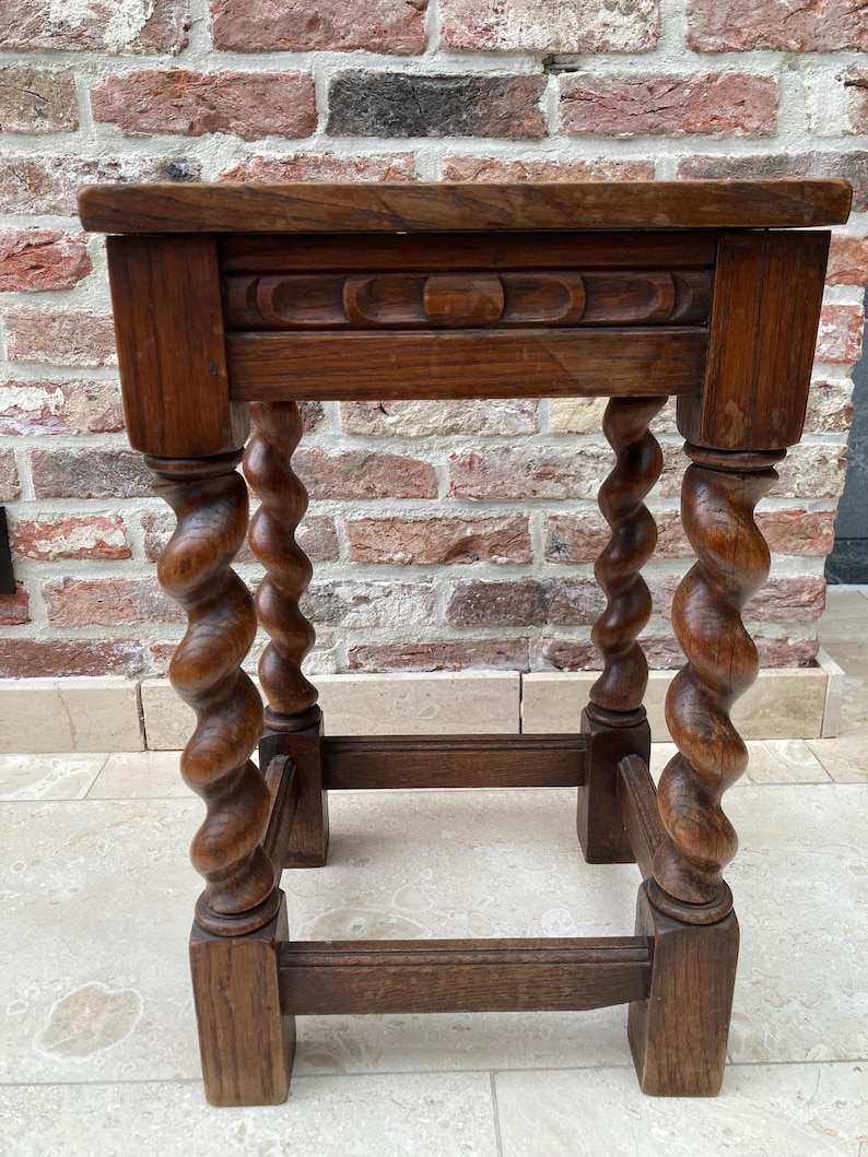 May include: A small, antique wooden side table with a dark brown finish. The table features a rectangular top, a carved apron, and four intricately carved, spiral-turned legs. The legs are connected by a lower stretcher for added stability.