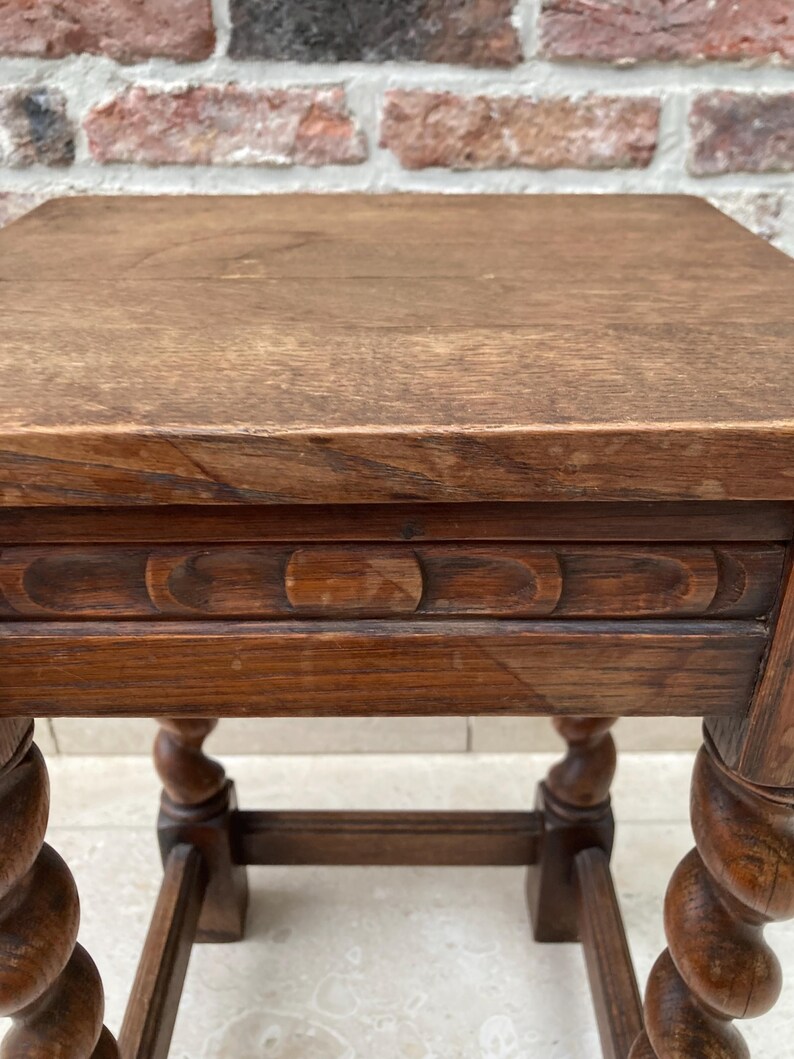 May include: A small, square, antique wooden table with a dark brown finish. The table features a carved apron and intricately turned legs. The tabletop is made of solid wood, showing the natural grain. The table is approximately 20 inches tall.