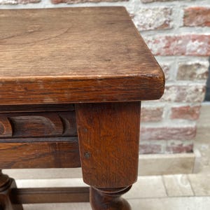 May include: Close-up of a small, antique wooden table with a dark brown finish. The table features a square top, carved detailing, and a twisted leg design. The wood grain is visible, adding to its vintage appeal.