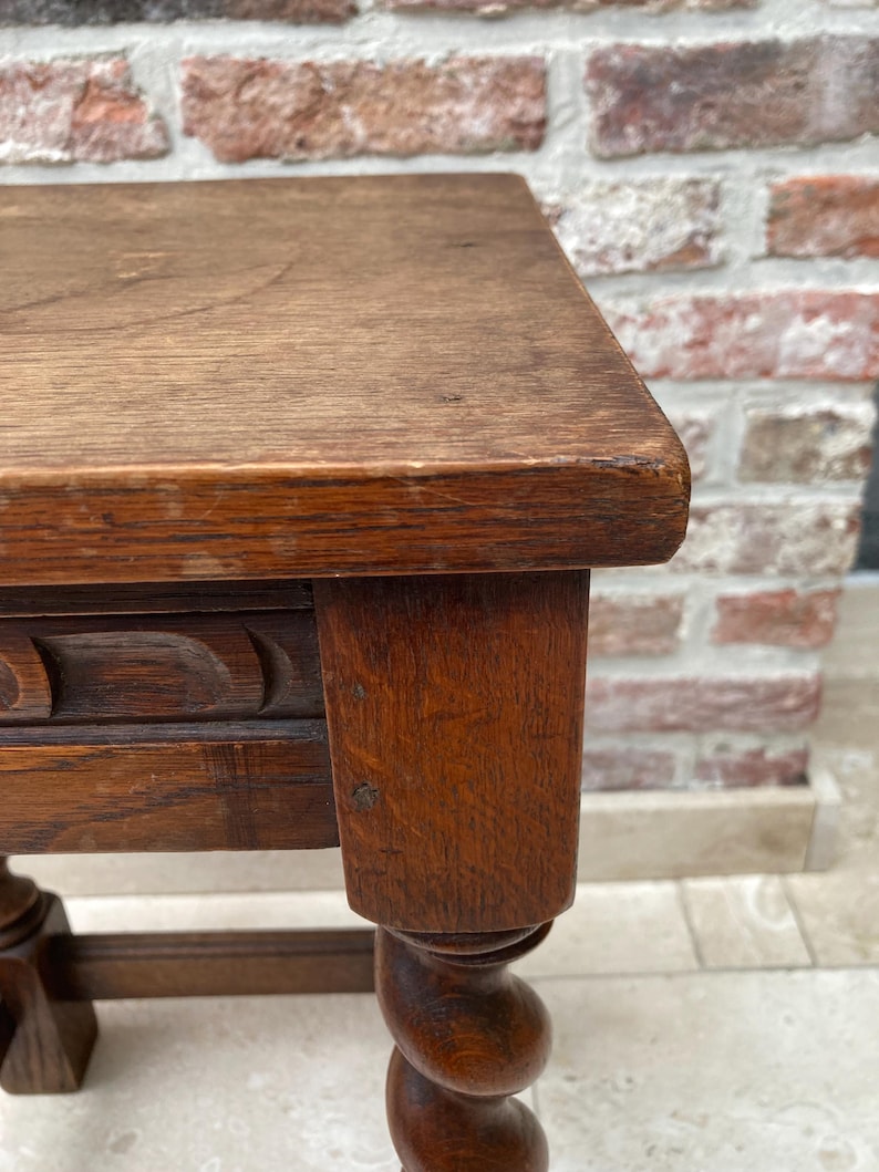 May include: Close-up of a small, antique wooden table with a dark brown finish. The table features a square top, carved detailing, and a twisted leg design. The wood grain is visible, adding to its vintage appeal.