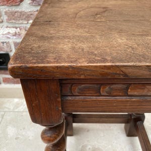 May include: A close-up of a small, antique wooden table. The table has a rectangular top and a carved apron. One leg is a turned spiral design. The wood has a warm, brown tone and visible grain.