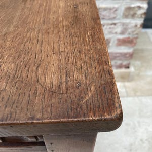 May include: Close-up of a wooden table with a dark brown finish. The table's surface shows visible wood grain and a few small imperfections. The table has a rounded edge and a turned leg.