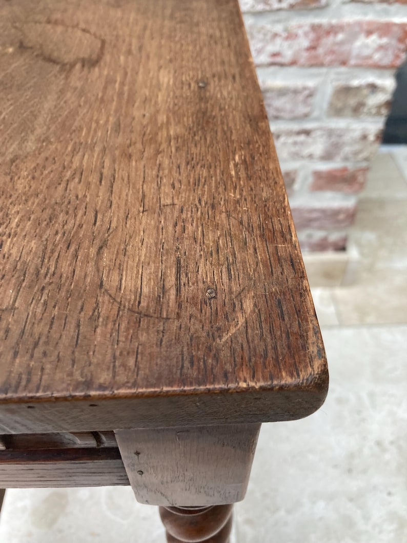 May include: Close-up of a wooden table with a dark brown finish. The table's surface shows visible wood grain and a few small imperfections. The table has a rounded edge and a turned leg.