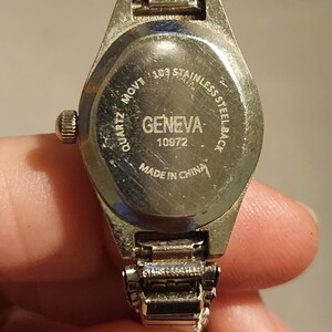 May include: Close-up of a Geneva quartz watch. The watch has a stainless steel back and a silver-tone metal band. The watch face is not visible. The back of the watch has the text "GENEVA" and "MADE IN CHINA".