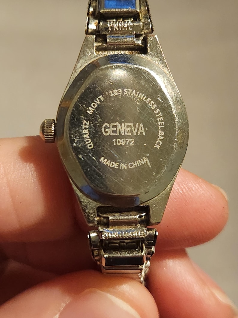 May include: Close-up of a Geneva quartz watch. The watch has a stainless steel back and a silver-tone metal band. The watch face is not visible. The back of the watch has the text "GENEVA" and "MADE IN CHINA".