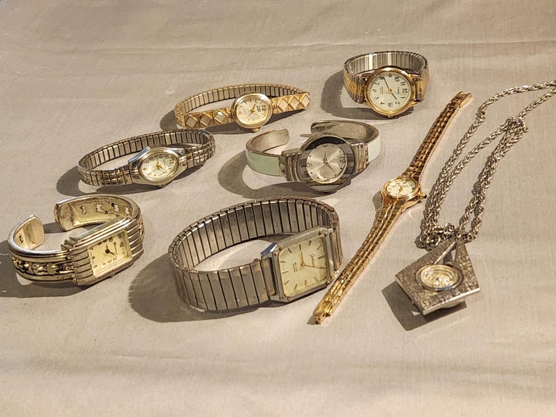May include: A collection of various wristwatches and a pendant watch. The watches feature gold and silver tones, with different band styles including stretch, cuff, and link bands. The watch faces are primarily round or rectangular.