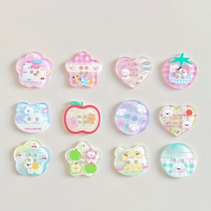 May include: A collection of twelve decorative buttons in various shapes, including flowers, hearts, and apples. Each button features a cute cartoon animal design in pastel colors, with a glossy finish. The buttons are ideal for crafts and sewing projects.
