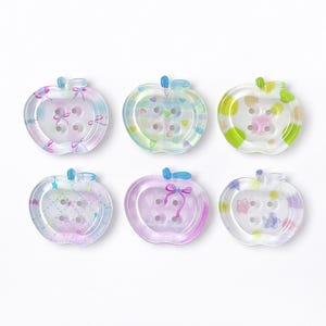 Può includere: Sei bottoni traslucidi a forma di mela in vari colori pastello. Ogni bottone ha un dettaglio a fiocco e quattro fori per cucire. I bottoni sono decorati con cuori e stelle.