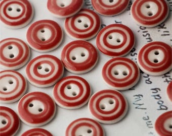 May include: A collection of red and white ceramic buttons with two holes each. The buttons have a white center with a red ring around it, and another red ring around the outer edge.
