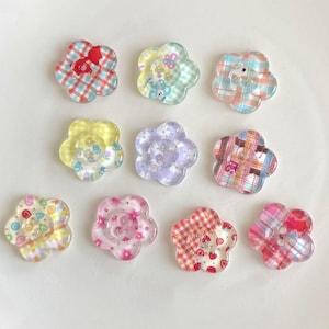 Peut inclure: Collection de dix embellissements en résine en forme de fleur. Chaque fleur présente un motif à carreaux ou à motifs différent dans diverses couleurs, dont le rouge, le bleu, le jaune et le rose. Certains ont de petits éléments décoratifs au centre.