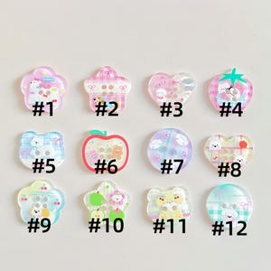 May include: A collection of twelve assorted acrylic buttons in various shapes including flowers, hearts, circles, and apples. Each button features colorful cartoon illustrations of puppies, bears, and fruit, labeled with numbers one through twelve.