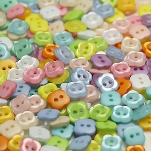 Peut inclure: Un assortiment de boutons colorés en forme de fleurs et carrés, dans diverses teintes pastel. Les boutons sont dans des tons de rose, jaune, bleu, vert et orange. Les boutons ont deux ou quatre trous pour la couture.