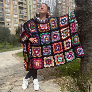 May include: A colorful crochet poncho with a black background and a high neck. The poncho is made of squares of different colors, including red, green, blue, yellow, and pink.