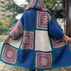 Puede incluir: Una chaqueta de punto de ganchillo azul, blanca y verde con capucha. La chaqueta está hecha de cuadrados con patrones circulares de colores.