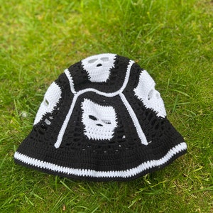 May include: Black and white crocheted bucket hat with a skull design. The hat has a white brim and a black crown with white skull shapes.