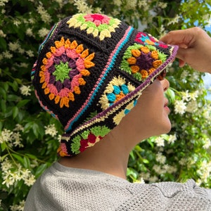 May include: A crocheted bucket hat with a colourful geometric pattern. The hat is made with black yarn and features a variety of colours, including pink, orange, yellow, green, and blue.