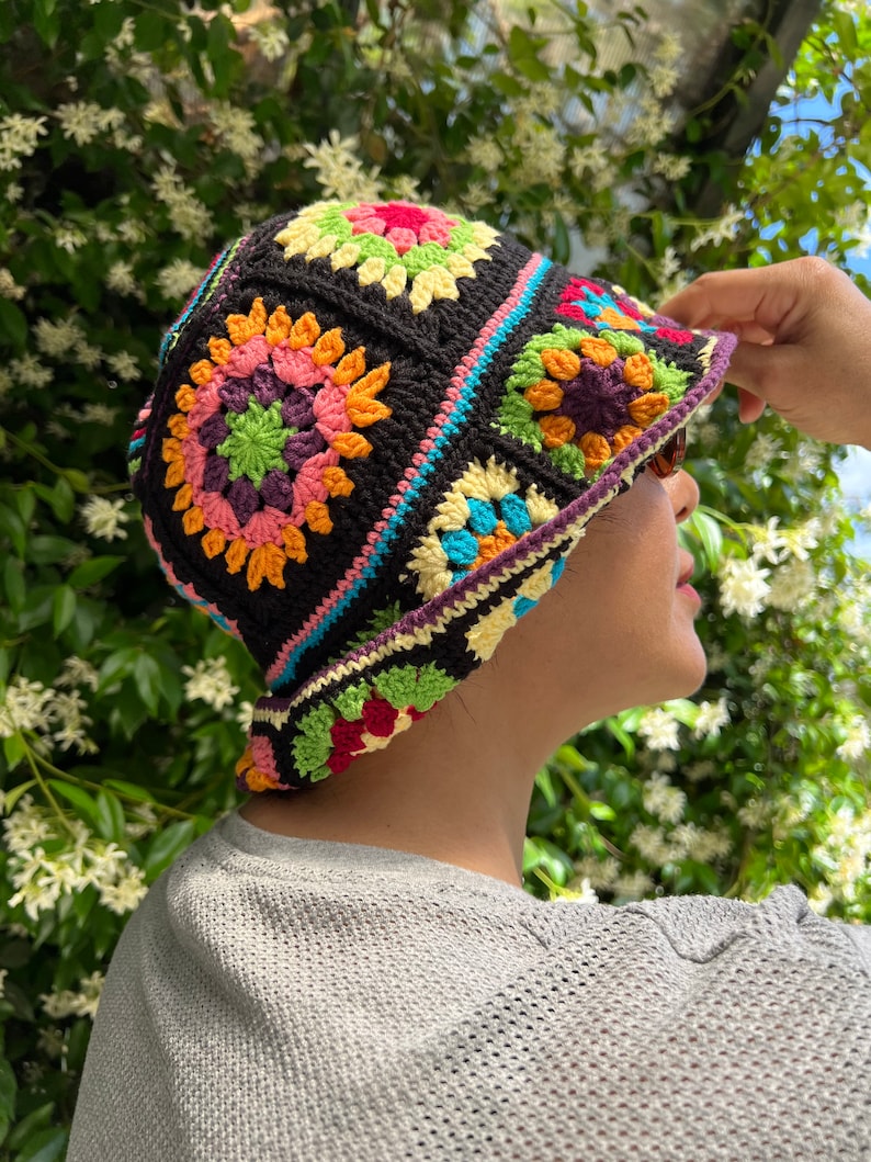 May include: A crocheted bucket hat with a colourful geometric pattern. The hat is made with black yarn and features a variety of colours, including pink, orange, yellow, green, and blue.