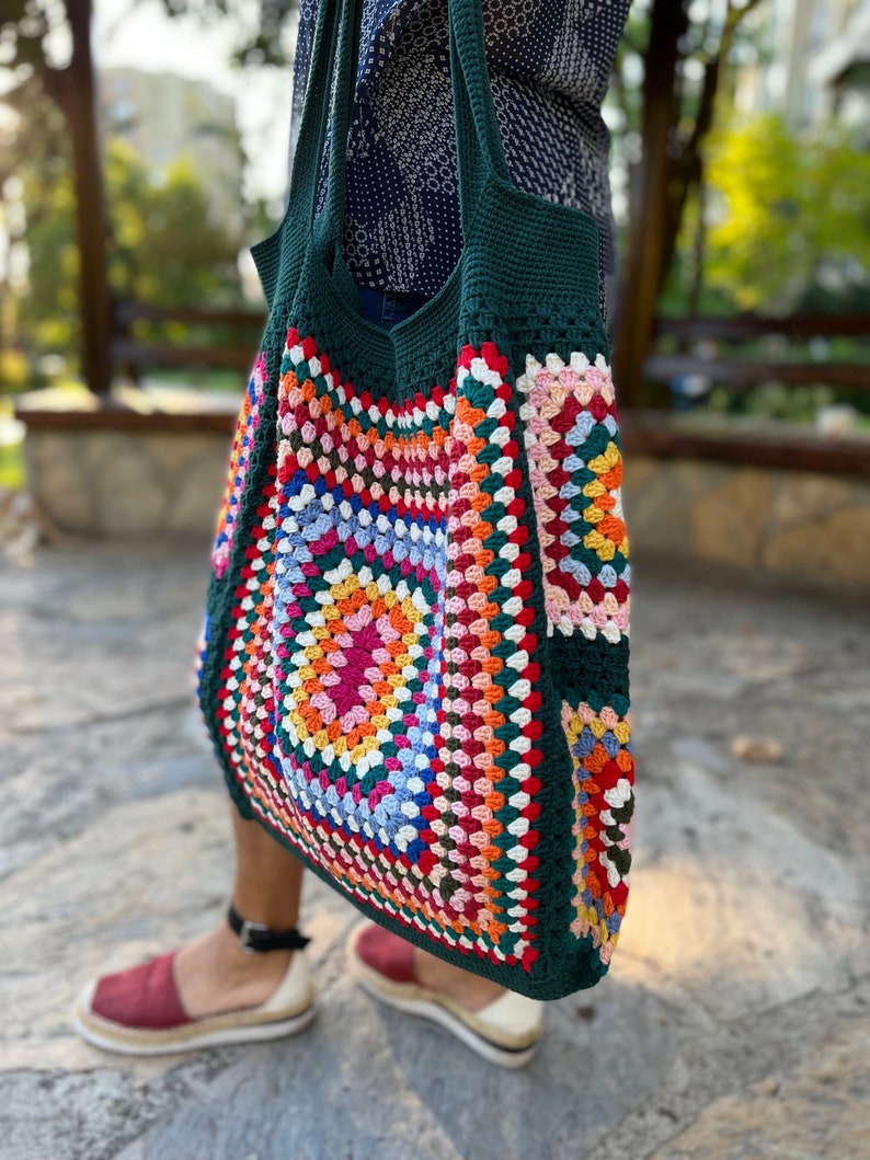 May include: A green crochet tote bag with a colorful granny square design. The bag has a wide, open top and two long straps.