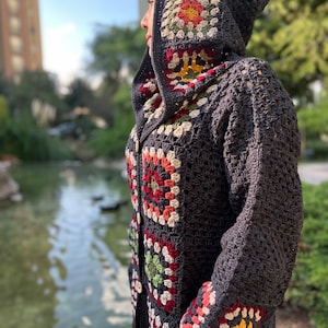 May include: A gray crocheted cardigan with a hood featuring colorful granny squares. The cardigan has a button closure and pockets.
