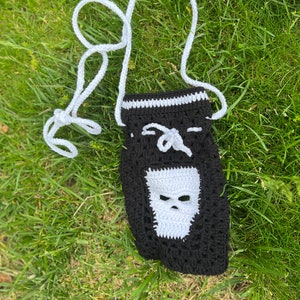 May include: A black crocheted bag with a white skull design. The bag has a white crocheted strap.