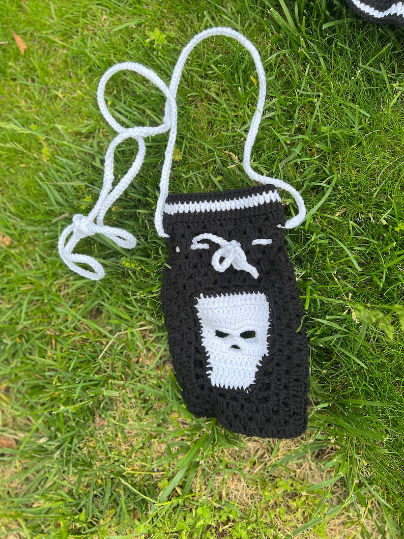 May include: A black crocheted bag with a white skull design. The bag has a white crocheted strap.