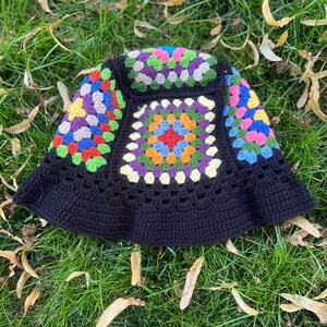 May include: A black crochet bucket hat featuring a colourful granny square pattern. The hat has a wide brim and is crafted from a soft, textured yarn.
