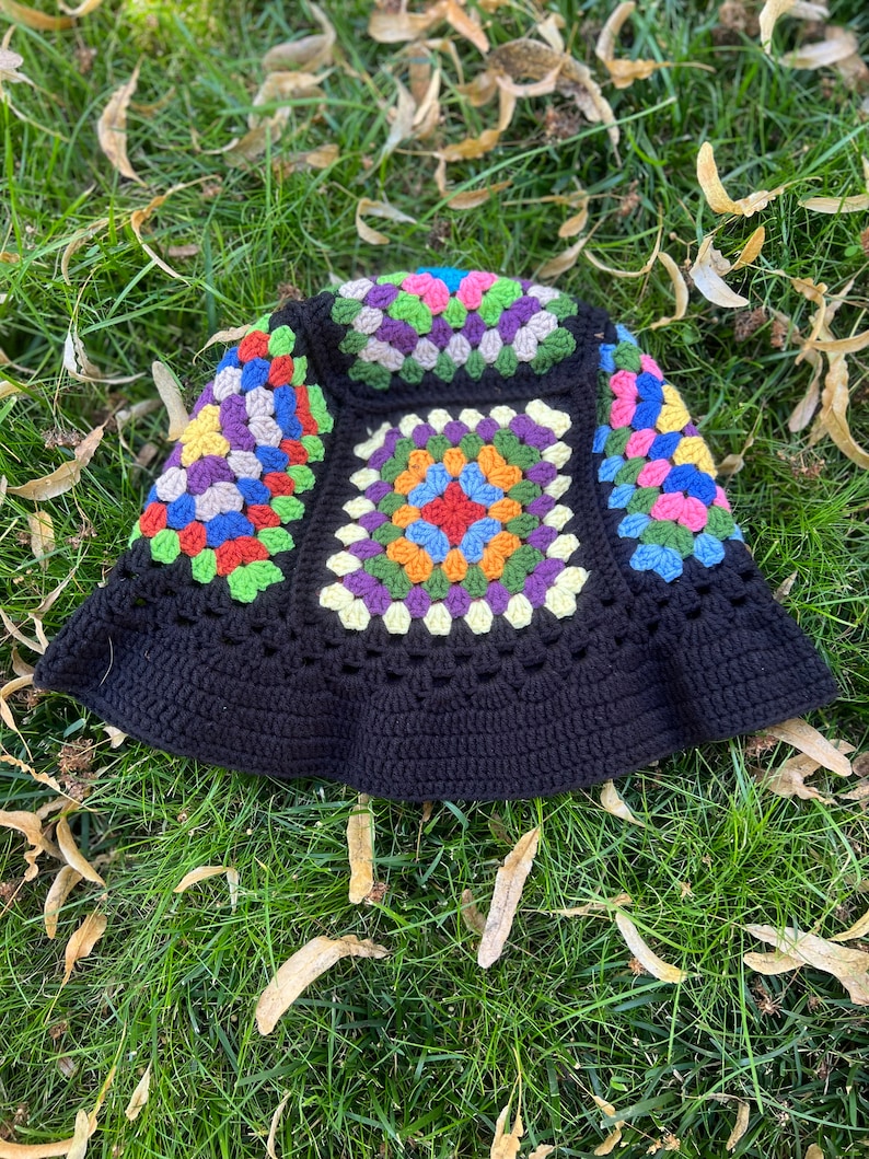 May include: A black crochet bucket hat featuring a colourful granny square pattern. The hat has a wide brim and is crafted from a soft, textured yarn.