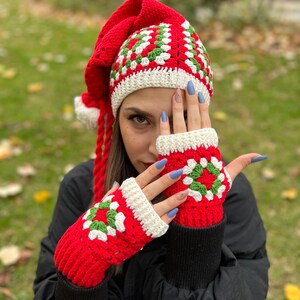 May include: Red and green crochet hat with a long tail and matching fingerless gloves. The hat has a white crocheted brim and the gloves have a white crocheted cuff.