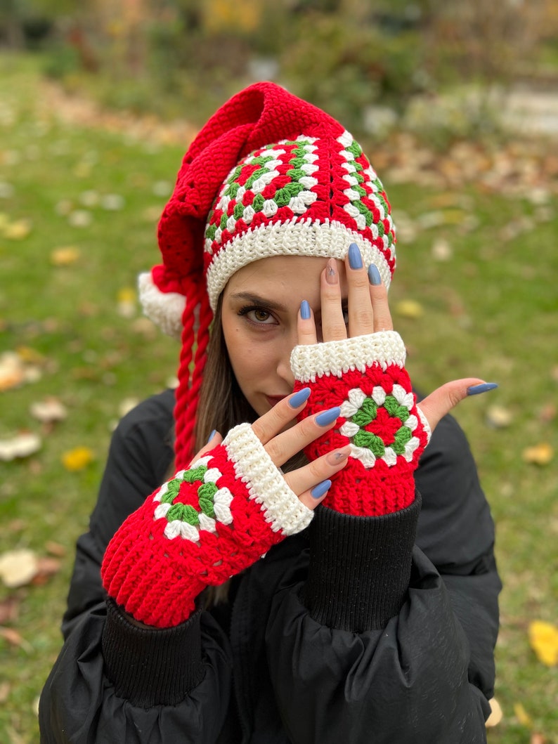 May include: Red and green crochet hat with a long tail and matching fingerless gloves. The hat has a white crocheted brim and the gloves have a white crocheted cuff.