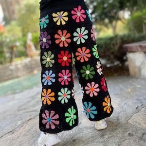 May include: Wide-leg crochet trousers with a black background and colourful daisy-shaped flowers.