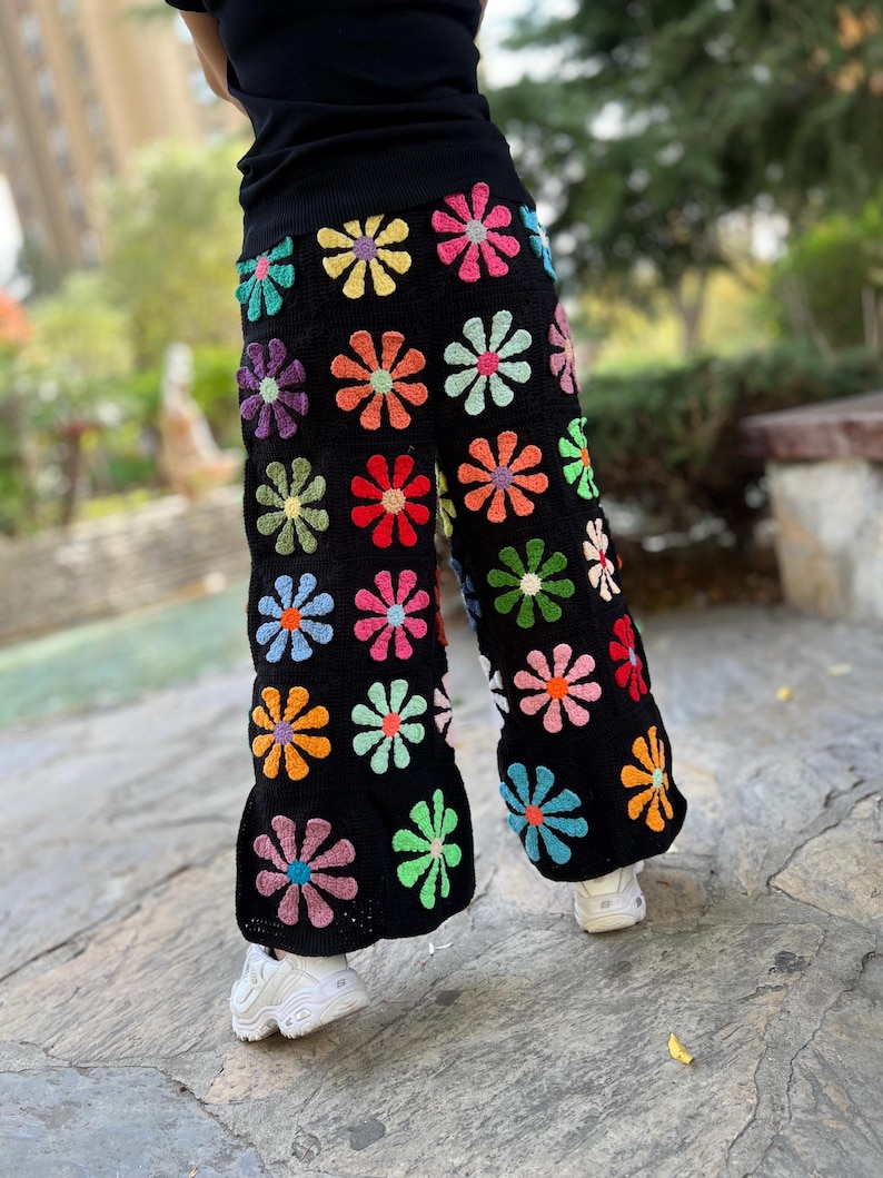 May include: Wide-leg crochet trousers with a black background and colourful daisy-shaped flowers.