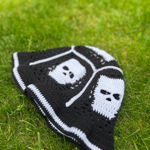 May include: Black and white crocheted bucket hat with skull designs. The hat has a white brim and a black crown with white skull designs.