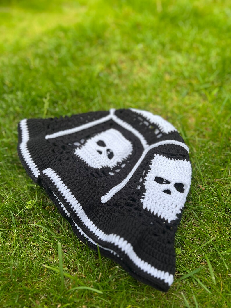 May include: Black and white crocheted bucket hat with skull designs. The hat has a white brim and a black crown with white skull designs.