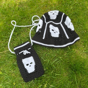 May include: A black and white crocheted bucket hat with a skull design and a matching black and white crocheted bag with a skull design.