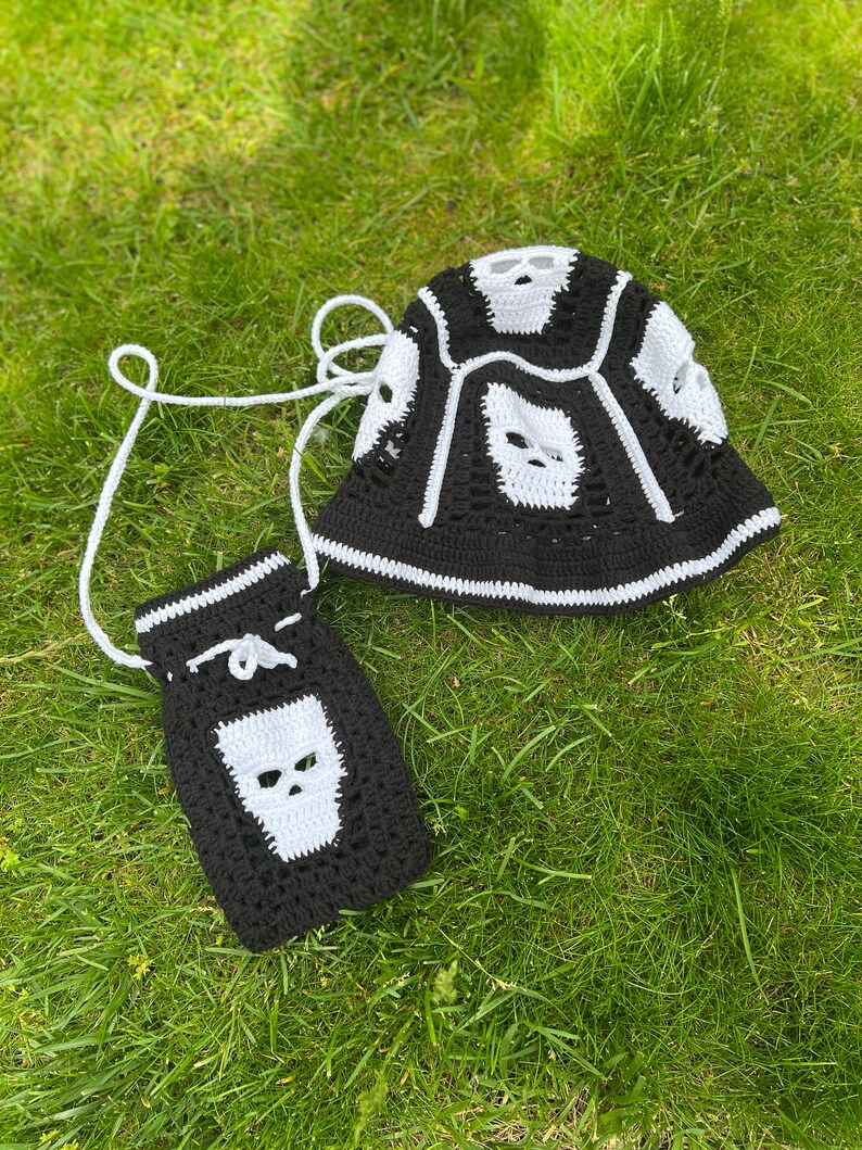May include: A black and white crocheted bucket hat with a skull design and a matching black and white crocheted bag with a skull design.