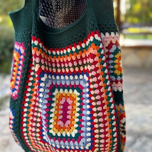 May include: A green crochet tote bag with a colorful granny square design. The bag has a large, square shape and is made with a thick yarn.