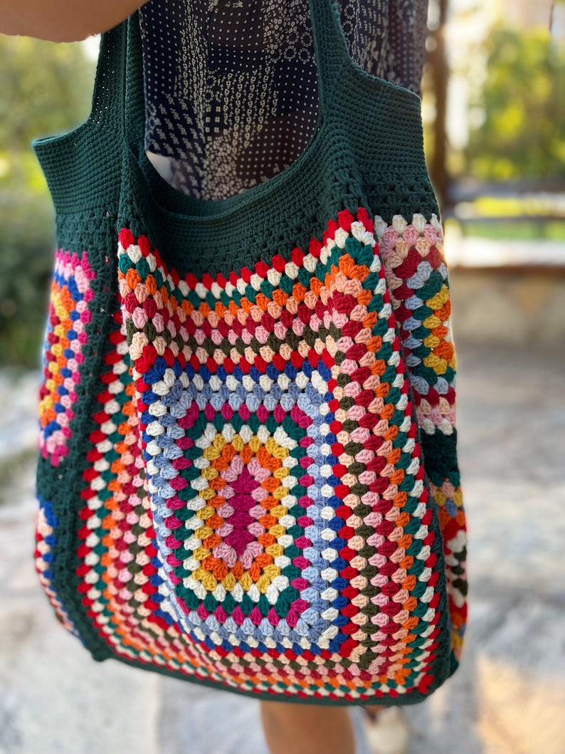 May include: A green crochet tote bag with a colorful granny square design. The bag has a large, square shape and is made with a thick yarn.