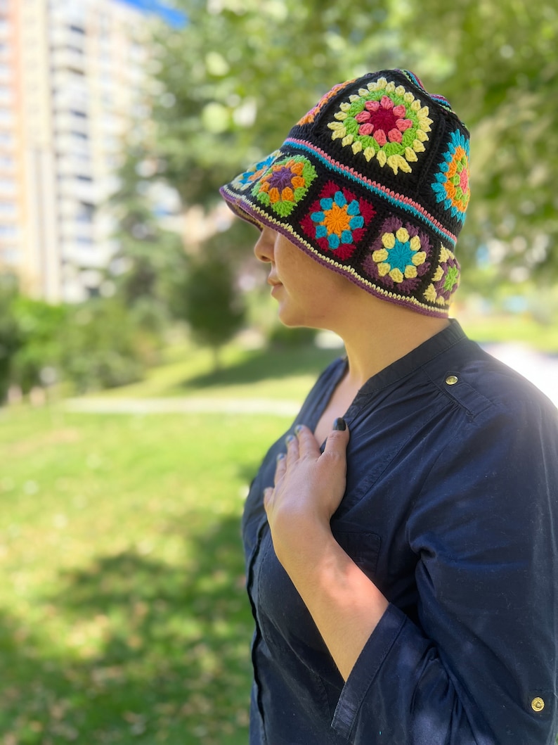May include: A black crochet bucket hat featuring colourful granny square designs. The hat has a wide brim and is crafted using a range of colours, including red, orange, yellow, green, blue, and purple.