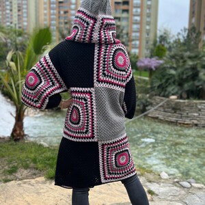 May include: A long black crochet cardigan with a hood, featuring a patchwork design of colorful squares. The cardigan has a relaxed fit and is made with a soft, chunky yarn.