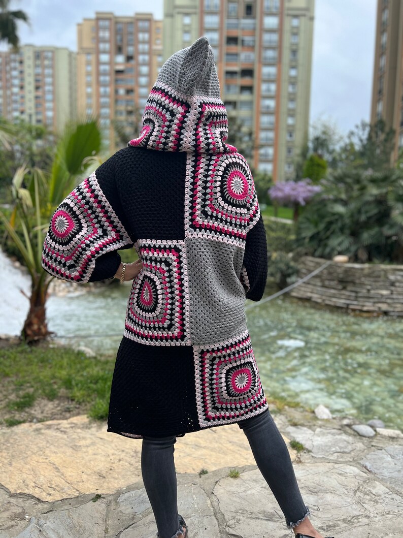May include: A long black crochet cardigan with a hood, featuring a patchwork design of colorful squares. The cardigan has a relaxed fit and is made with a soft, chunky yarn.