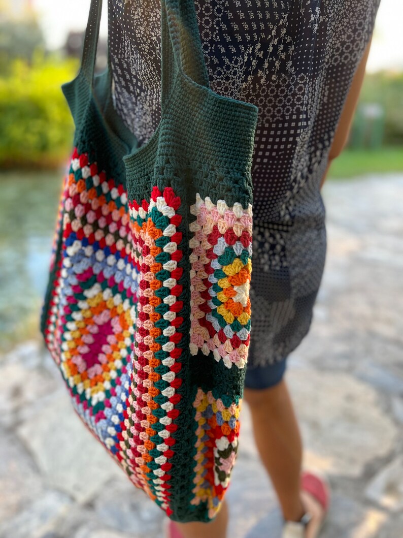May include: A green crochet tote bag with a colorful granny square pattern. The bag has a long strap and is made of thick yarn.