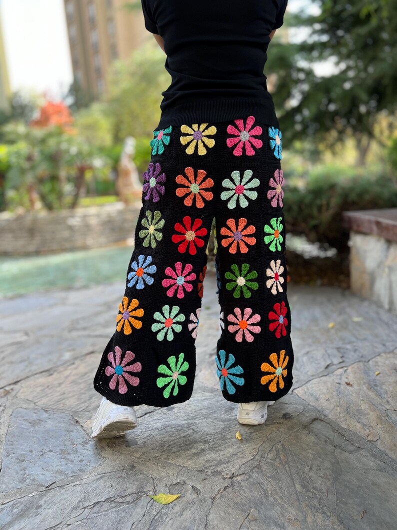 May include: Black crochet trousers with a colourful daisy pattern. The trousers are wide-legged and have a relaxed fit.
