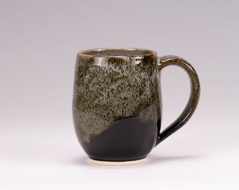 May include: A ceramic mug with a dark green and black glaze. The mug has a rounded body and a handle.