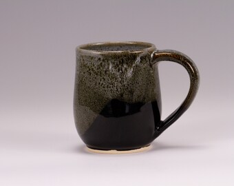May include: A ceramic mug with a black and green glaze. The mug has a rounded body and a handle.