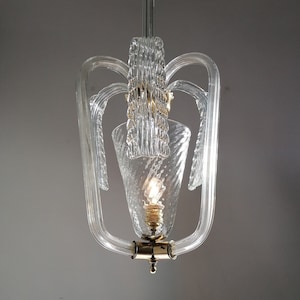 May include: A clear glass chandelier with a gold-toned metal base and a single light bulb. The chandelier has a unique design with multiple curved glass arms.